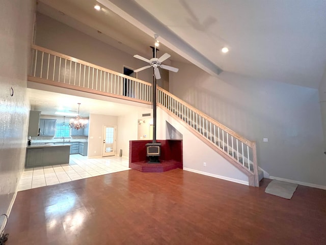 unfurnished living room with a wood stove, sink, ceiling fan, beamed ceiling, and light hardwood / wood-style floors