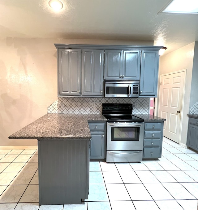 kitchen featuring kitchen peninsula, backsplash, dark stone counters, stainless steel appliances, and light tile patterned floors