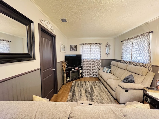 living room featuring a textured ceiling, a wainscoted wall, wood finished floors, visible vents, and crown molding