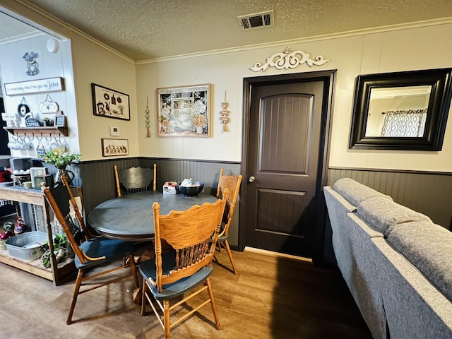 dining space featuring a wainscoted wall, crown molding, visible vents, a textured ceiling, and wood finished floors