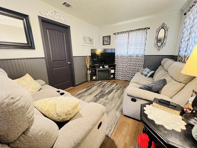 living area with visible vents, a wainscoted wall, wood finished floors, crown molding, and a textured ceiling