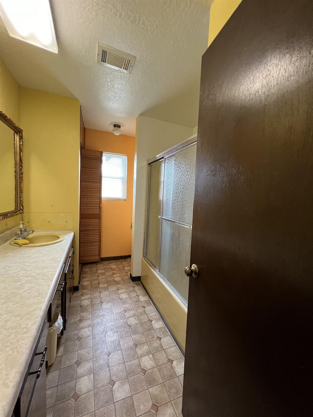 bathroom with shower / bath combination with glass door, a textured ceiling, vanity, and baseboards
