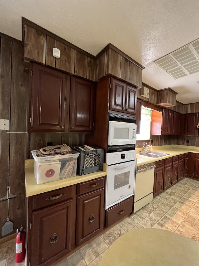 kitchen featuring white appliances, a sink, light countertops, a textured ceiling, and dark brown cabinetry