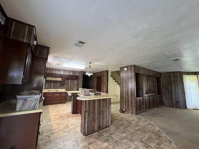 kitchen featuring light countertops, wood walls, a kitchen island, under cabinet range hood, and dark brown cabinets