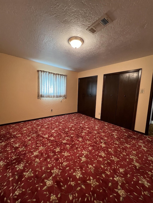 unfurnished bedroom featuring carpet, multiple closets, and a textured ceiling