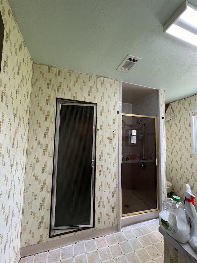 bathroom with wallpapered walls, a shower stall, toilet, baseboards, and a textured ceiling