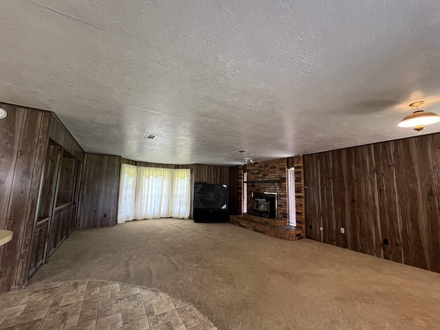 unfurnished living room featuring wooden walls, a fireplace, a textured ceiling, and carpet floors