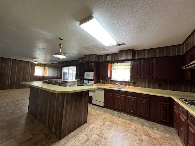 kitchen with white appliances, wood walls, light countertops, a sink, and a textured ceiling