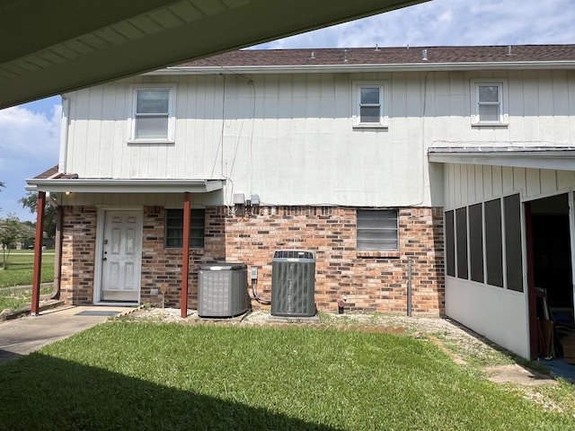 back of property with central AC unit, a yard, and brick siding