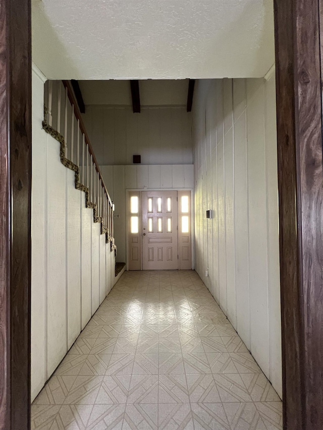 hall with stairway, light floors, beamed ceiling, and a textured ceiling