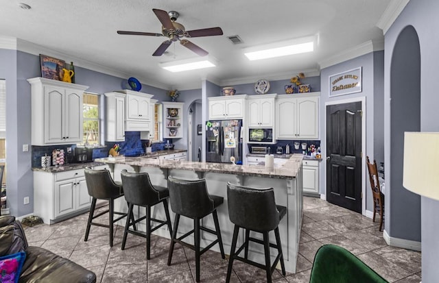 9655 Grapevine Dr, Orange, TX 77630 - kitchen with stainless steel fridge, arched walkways, a kitchen bar, ornamental molding, and black microwave