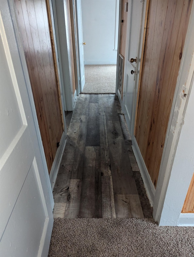 corridor featuring dark wood-type flooring and wooden walls