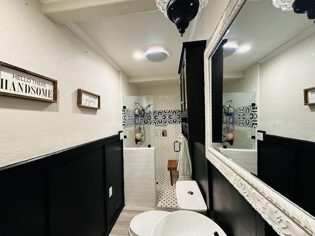 bathroom with hardwood / wood-style floors, toilet, a tile shower, and crown molding