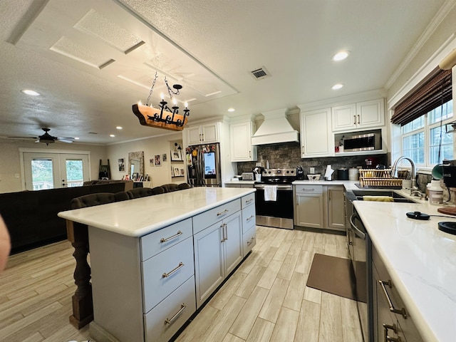 kitchen with french doors, custom range hood, stainless steel appliances, ceiling fan, and light hardwood / wood-style floors