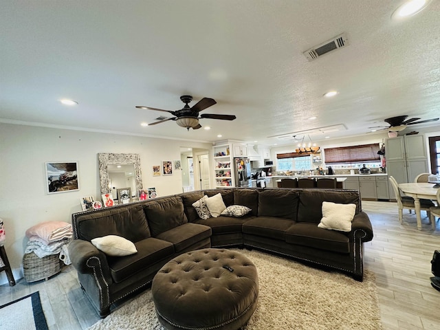 living room with light wood-type flooring, a textured ceiling, ceiling fan, and crown molding