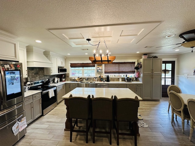 kitchen featuring stainless steel appliances, decorative light fixtures, gray cabinets, a kitchen island, and custom exhaust hood