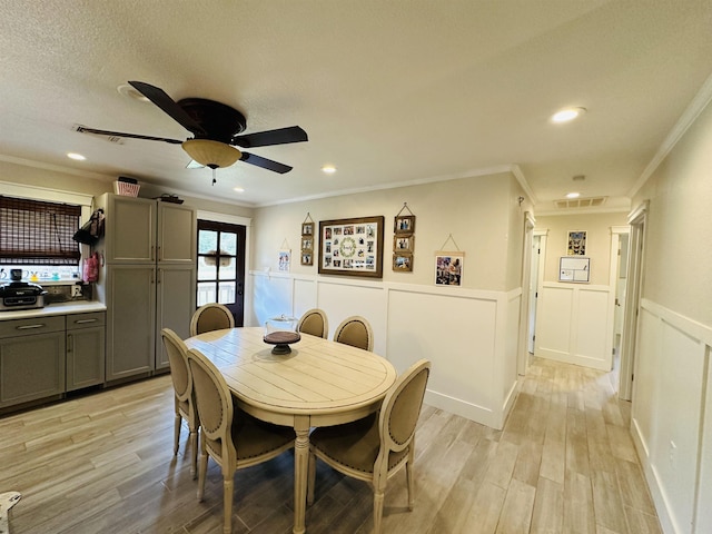 dining area with ceiling fan, light wood-type flooring, a textured ceiling, and ornamental molding