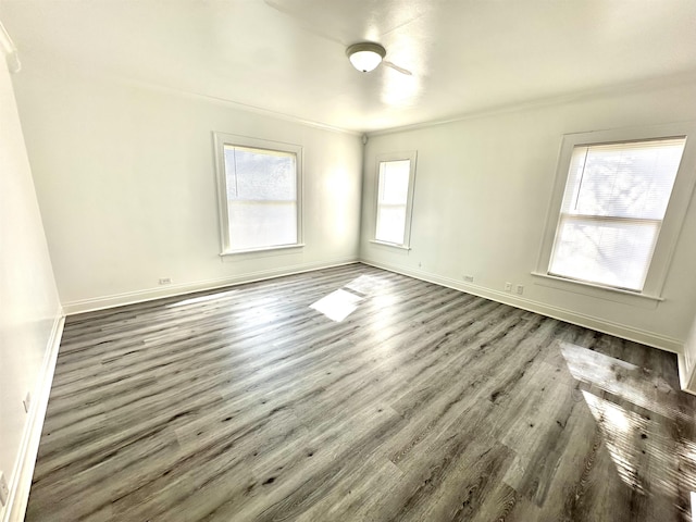 empty room with ornamental molding, a wealth of natural light, and dark wood-type flooring