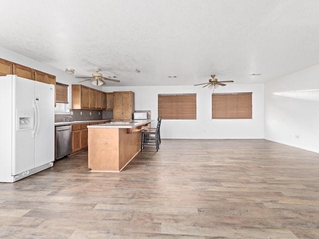 kitchen with a center island, white refrigerator with ice dispenser, stainless steel dishwasher, light wood-type flooring, and tasteful backsplash