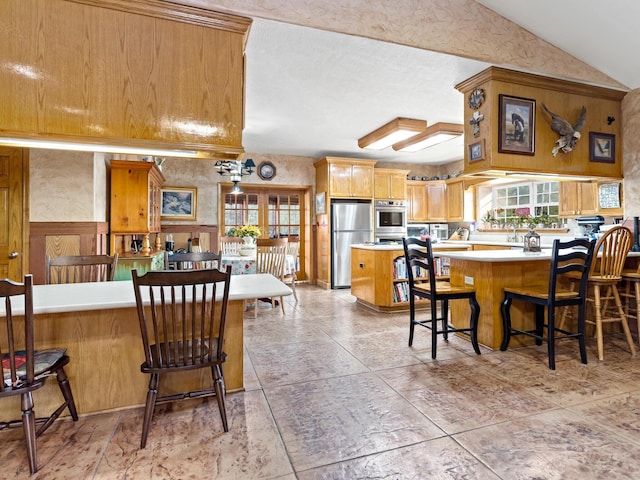 kitchen featuring a kitchen breakfast bar, kitchen peninsula, vaulted ceiling, and appliances with stainless steel finishes