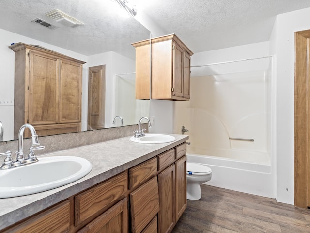 full bathroom featuring vanity, shower / washtub combination, toilet, a textured ceiling, and wood-type flooring