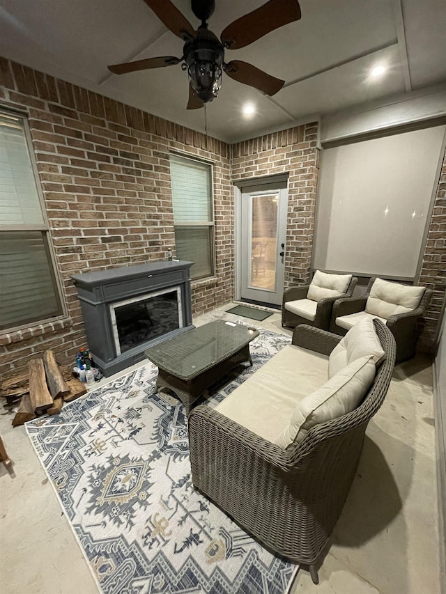 living room featuring a fireplace, ceiling fan, and brick wall