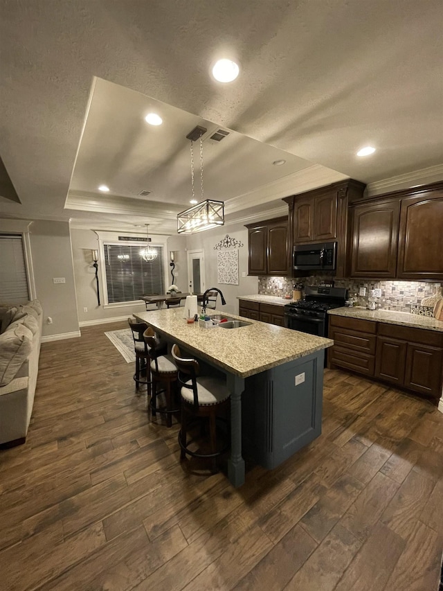 kitchen with sink, a kitchen island with sink, dark brown cabinets, gas stove, and a raised ceiling