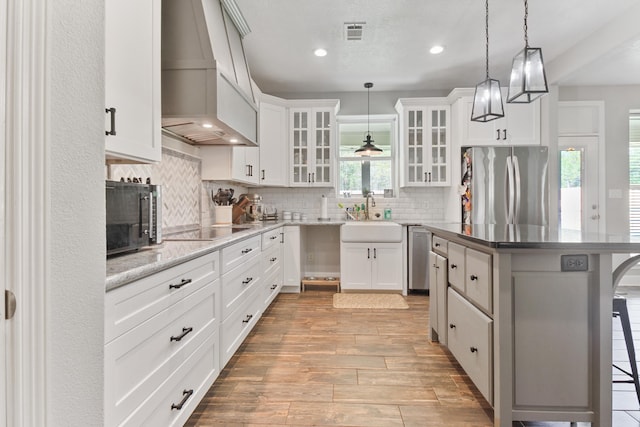 kitchen featuring a kitchen breakfast bar, white cabinetry, custom range hood, and black appliances