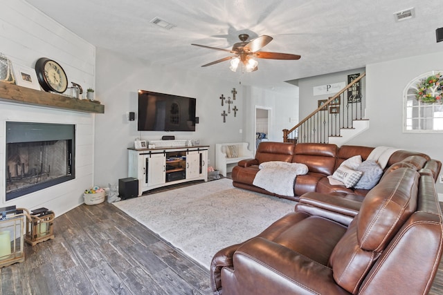 living room with a textured ceiling, ceiling fan, a fireplace, and dark hardwood / wood-style floors