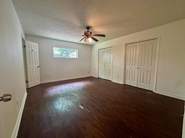 790 Pinchback Rd, Beaumont, TX 77707 - unfurnished bedroom featuring two closets, dark wood-style floors, a textured ceiling, baseboards, and a ceiling fan