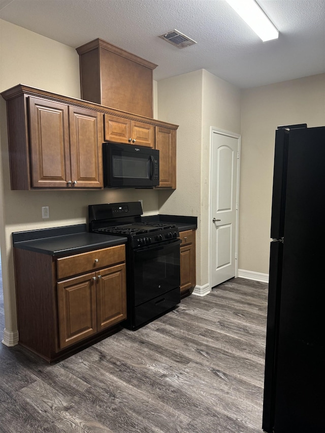 kitchen featuring dark hardwood / wood-style flooring, black appliances, and a textured ceiling