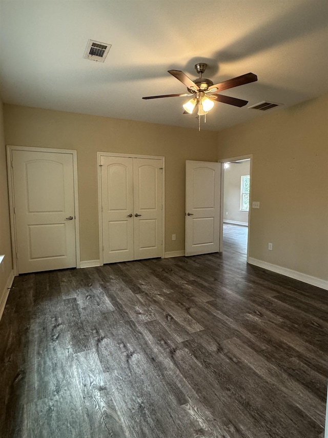 unfurnished bedroom featuring two closets, dark hardwood / wood-style floors, and ceiling fan