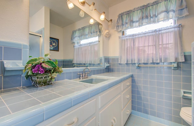 bathroom with tile patterned floors, toilet, vanity, a shower with shower door, and tile walls