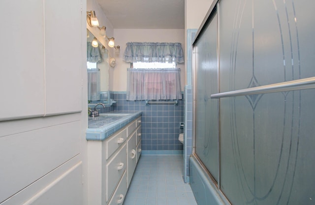 full bathroom featuring vanity, combined bath / shower with glass door, tile patterned flooring, toilet, and tile walls