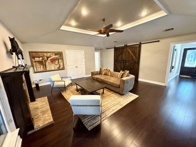 living room with dark hardwood / wood-style flooring, a barn door, a raised ceiling, and crown molding