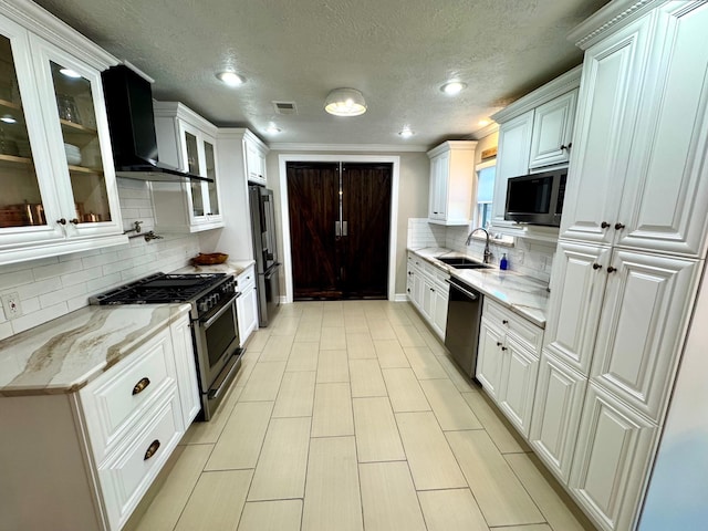 kitchen with light stone countertops, premium appliances, sink, wall chimney range hood, and white cabinetry