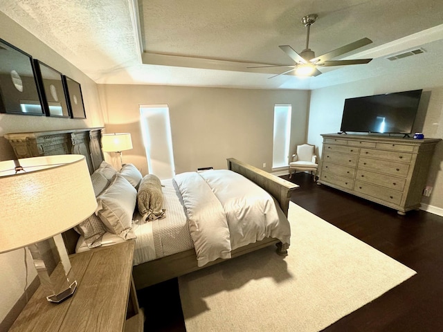 bedroom with a textured ceiling, dark hardwood / wood-style floors, ceiling fan, and a tray ceiling