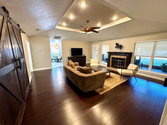 living room with a tile fireplace, dark wood-type flooring, a raised ceiling, a barn door, and a textured ceiling