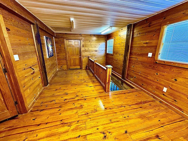 hallway with light wood finished floors, wood ceiling, wooden walls, and an upstairs landing