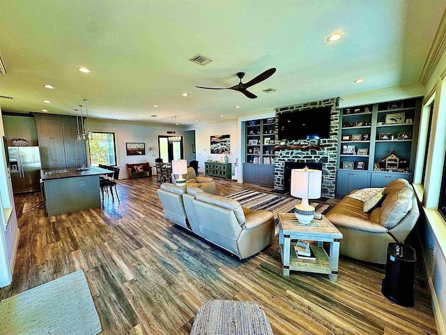living area featuring visible vents, crown molding, a fireplace, a ceiling fan, and dark wood finished floors