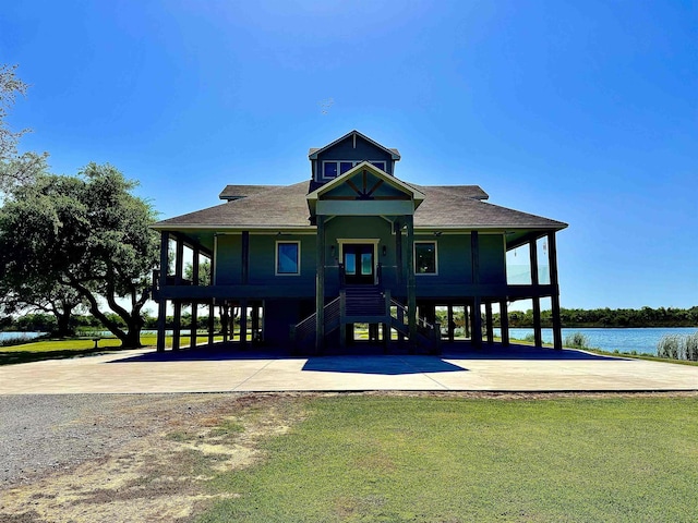 view of front of home featuring roof with shingles, stairway, a front yard, a water view, and driveway