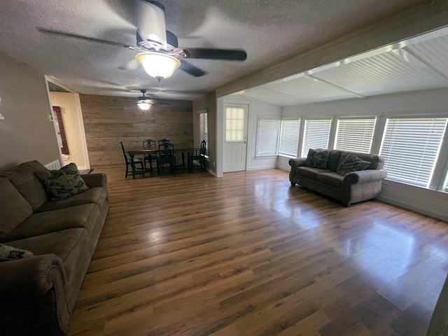 living room featuring a textured ceiling, ceiling fan, dark wood-type flooring, vaulted ceiling with beams, and wood walls