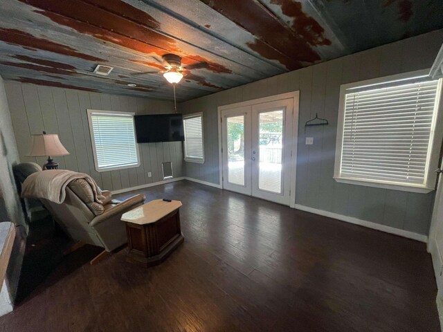 living area with dark hardwood / wood-style flooring, ceiling fan, french doors, and wood walls