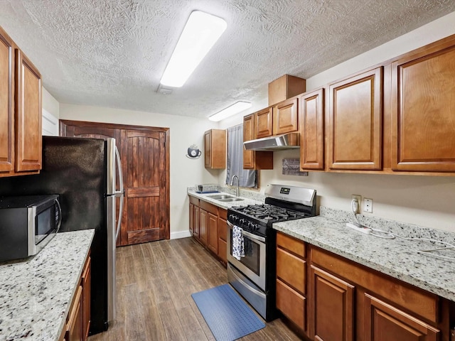 4015 42nd St, Port Arthur, TX 77642 - kitchen with appliances with stainless steel finishes, under cabinet range hood, dark wood-style flooring, a textured ceiling, and brown cabinetry