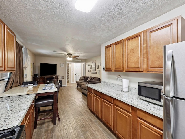 4015 42nd St, Port Arthur, TX 77642 - kitchen featuring appliances with stainless steel finishes, open floor plan, light wood-style floors, ceiling fan, and brown cabinets