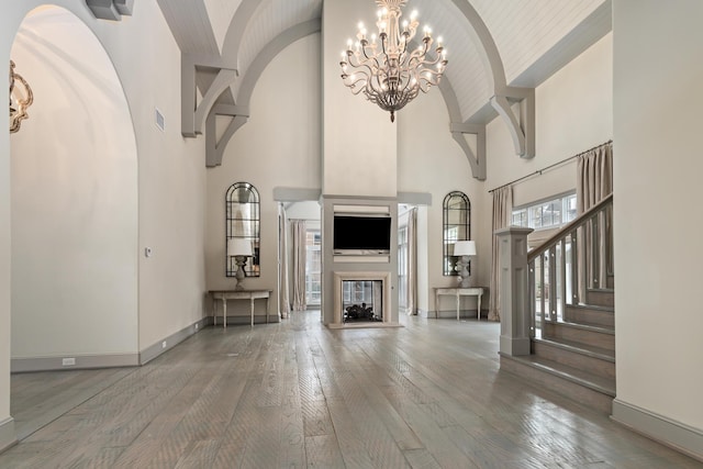 unfurnished living room with wood-type flooring, an inviting chandelier, and high vaulted ceiling