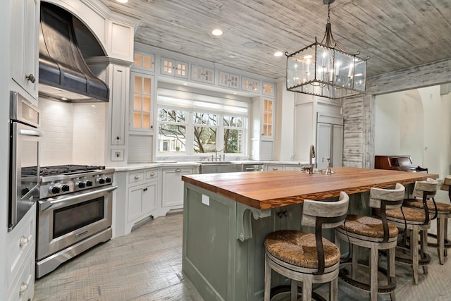 kitchen with appliances with stainless steel finishes, butcher block counters, white cabinetry, custom range hood, and a kitchen island