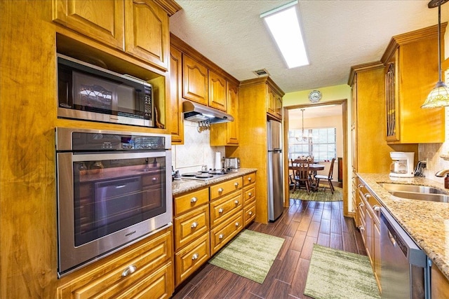 kitchen with light stone countertops, stainless steel appliances, sink, a notable chandelier, and hanging light fixtures