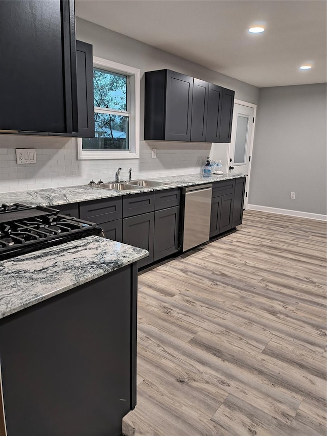 kitchen featuring stainless steel dishwasher, light stone counters, cooktop, sink, and light hardwood / wood-style floors