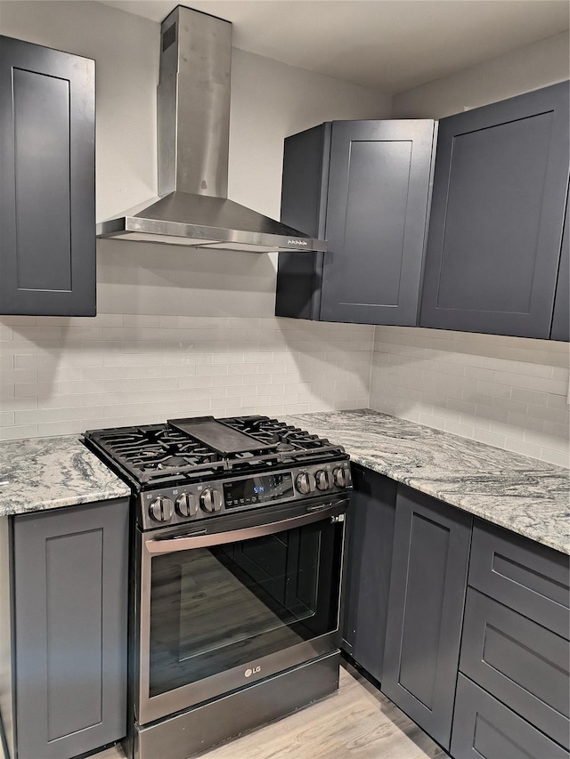 kitchen with gas stove, decorative backsplash, light stone counters, and wall chimney exhaust hood